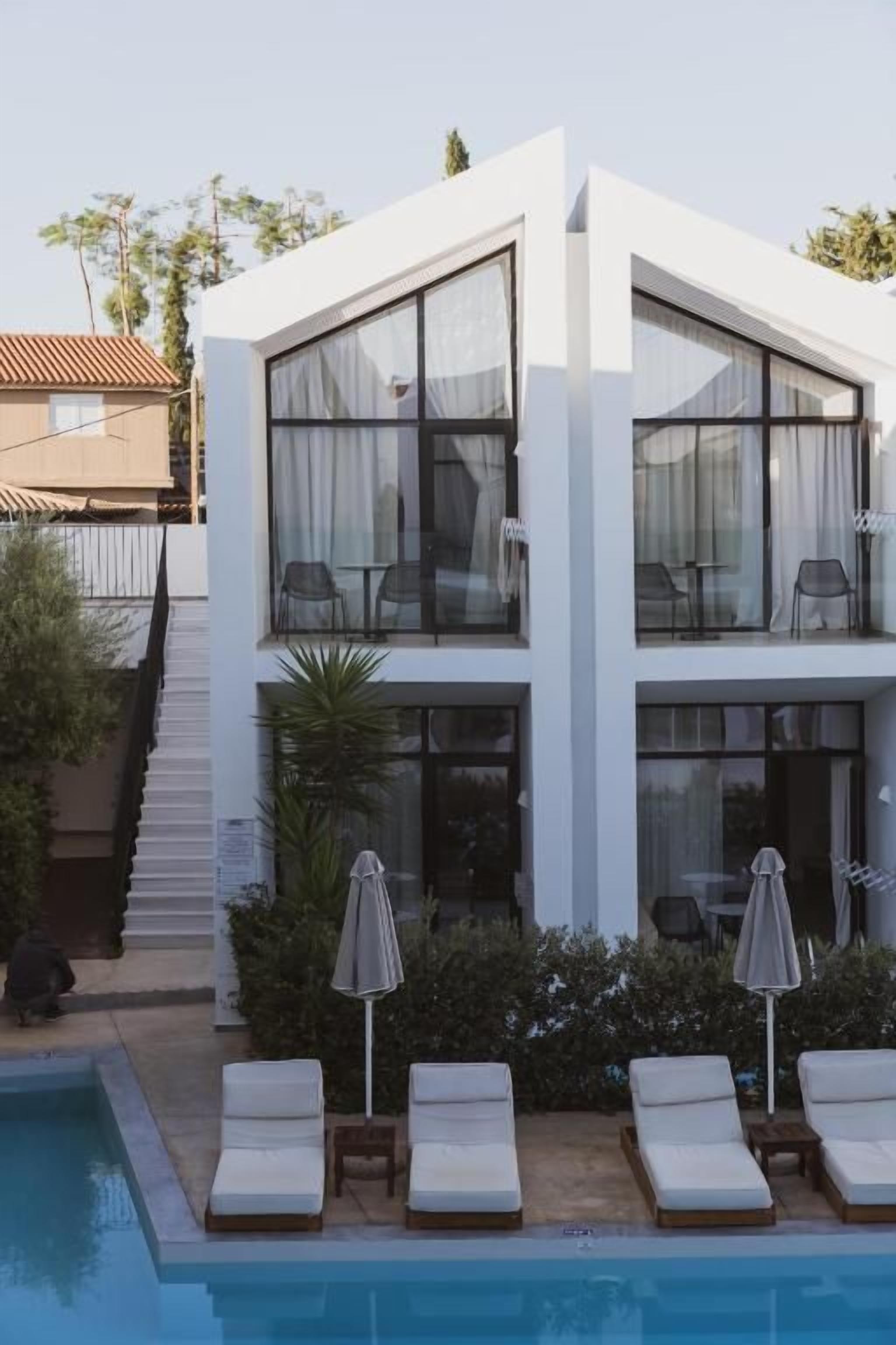 A modern two-story building with a swimming pool, lounge chairs, and umbrellas.