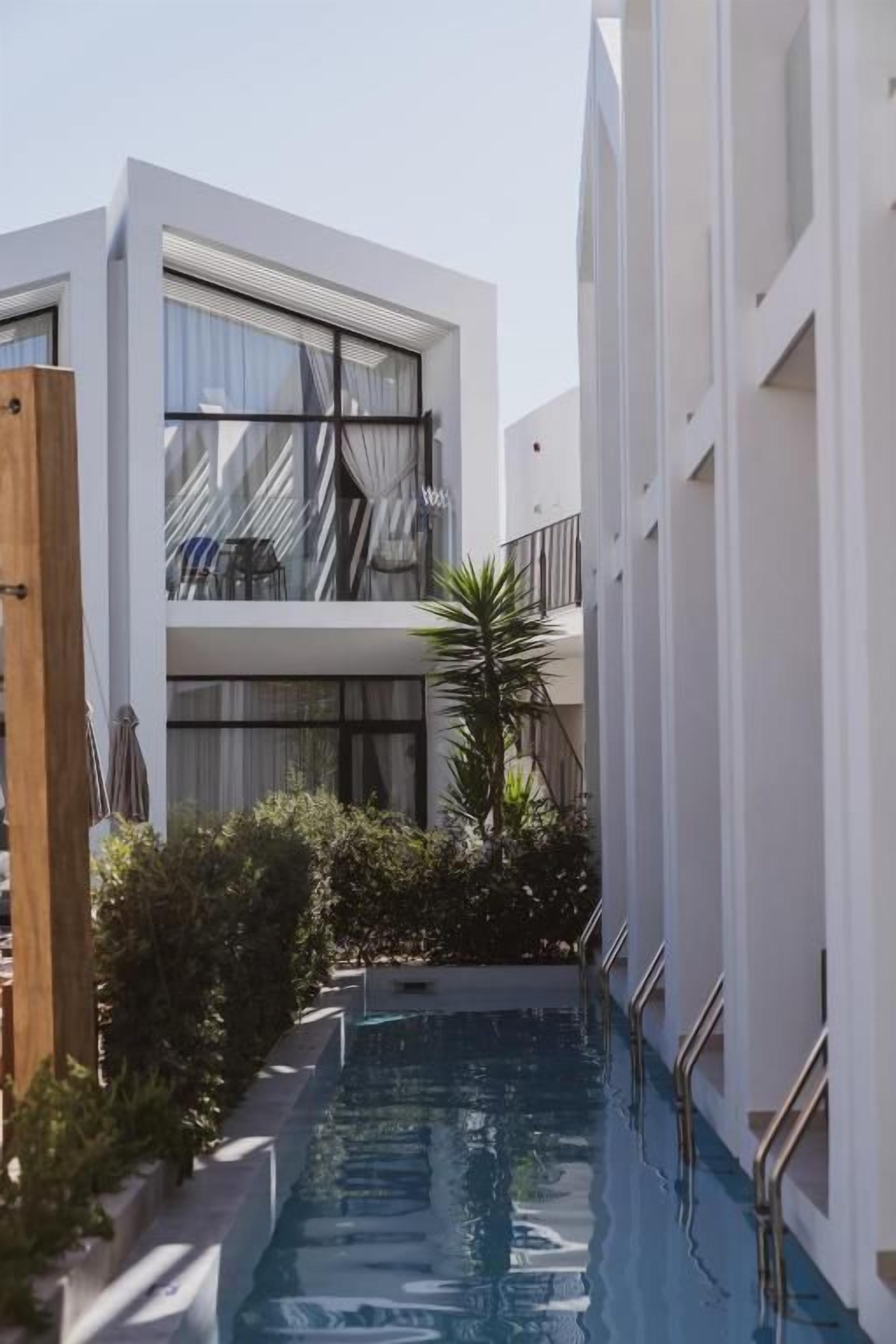 Un bâtiment moderne doté d’une piscine, d’un balcon avec des chaises et d’une porte en bois.