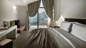 A modern hotel room with a large bed, a desk with a laptop, and a view of the cityscape through the window. - Cavo Vezal - Adults Only (Zakynthos)