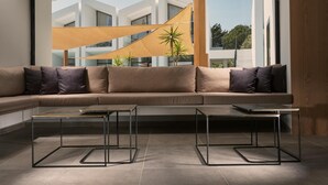 A modern living room with a large sectional sofa, two glass-top coffee tables, and a view of a building with a wooden structure outside. - Cavo Vezal - Adults Only (Zakynthos)
