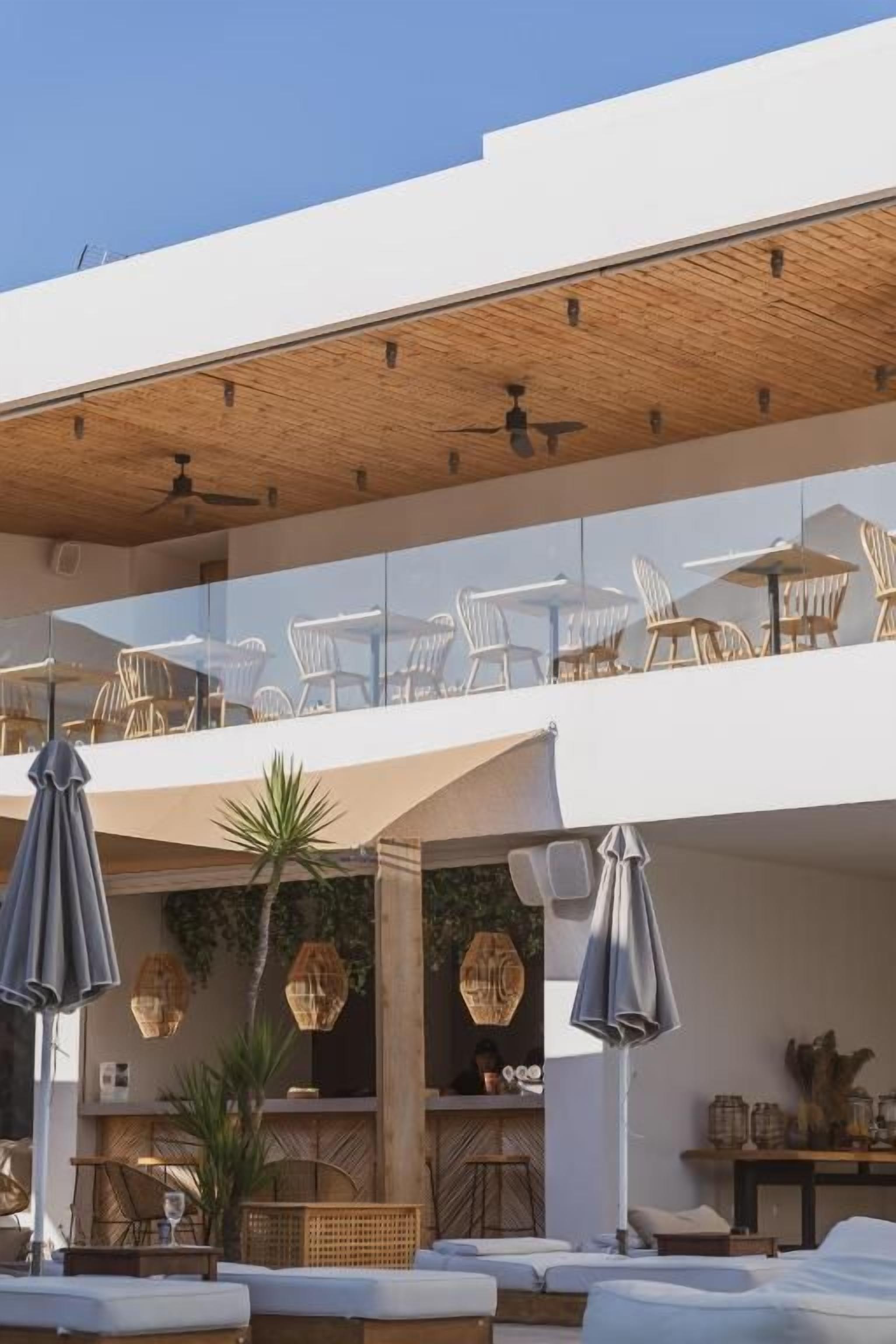 Uma área moderna de estar ao ar livre com espreguiçadeiras e guarda-sóis, teto de madeira e um bar com balcão.