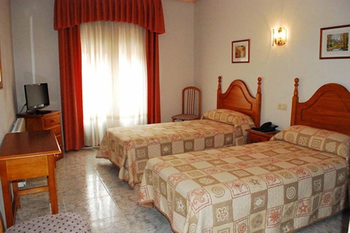 A hotel room with two beds, a desk, a chair, a television, and a window with curtains.