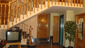 Una escalera con balaustres de madera, un televisor sobre un mueble bajo y una planta en maceta.
