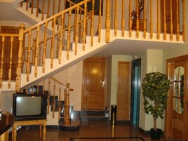 Una escalera con balaustres de madera, un televisor sobre un mueble bajo y una planta en maceta.
