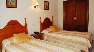 A hotel room with two wooden beds, a nightstand, a wall-mounted lamp, and a wooden wardrobe.