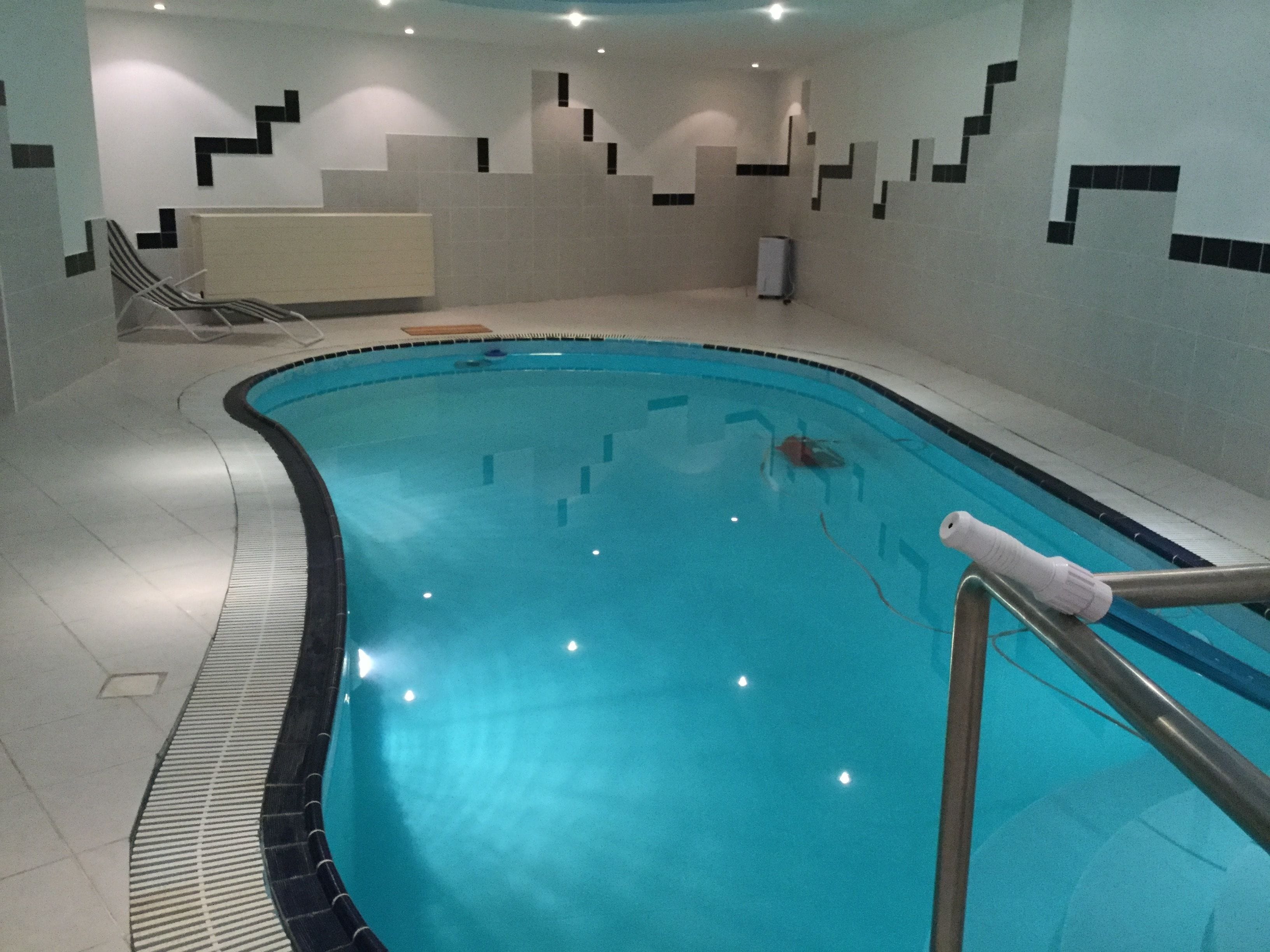 Una piscina interior con agua cristalina, un trampolín y una pared de azulejos con un diseño geométrico.