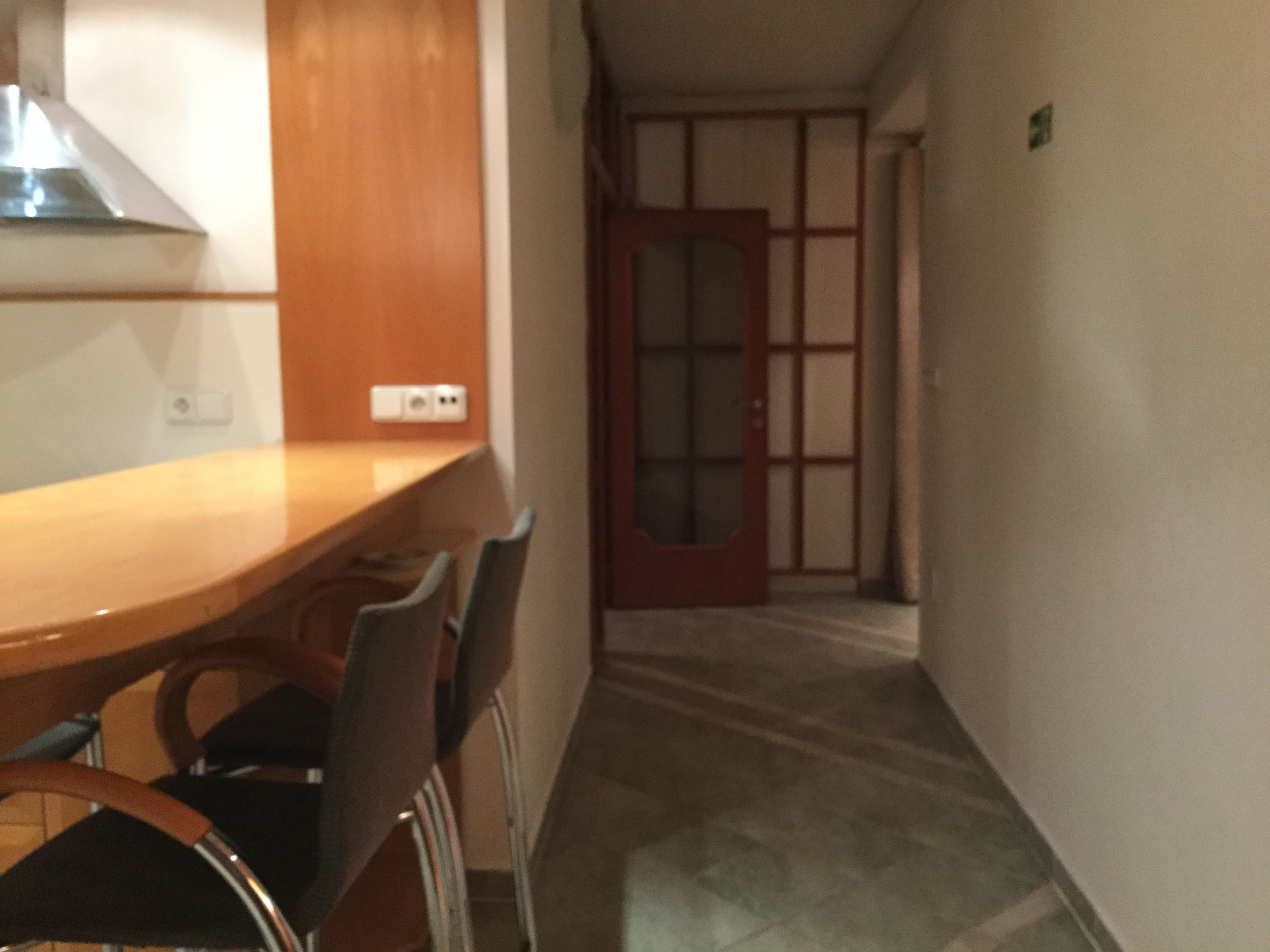 A hallway with a wooden table and chairs, a door with a glass panel, and a light switch on the wall.