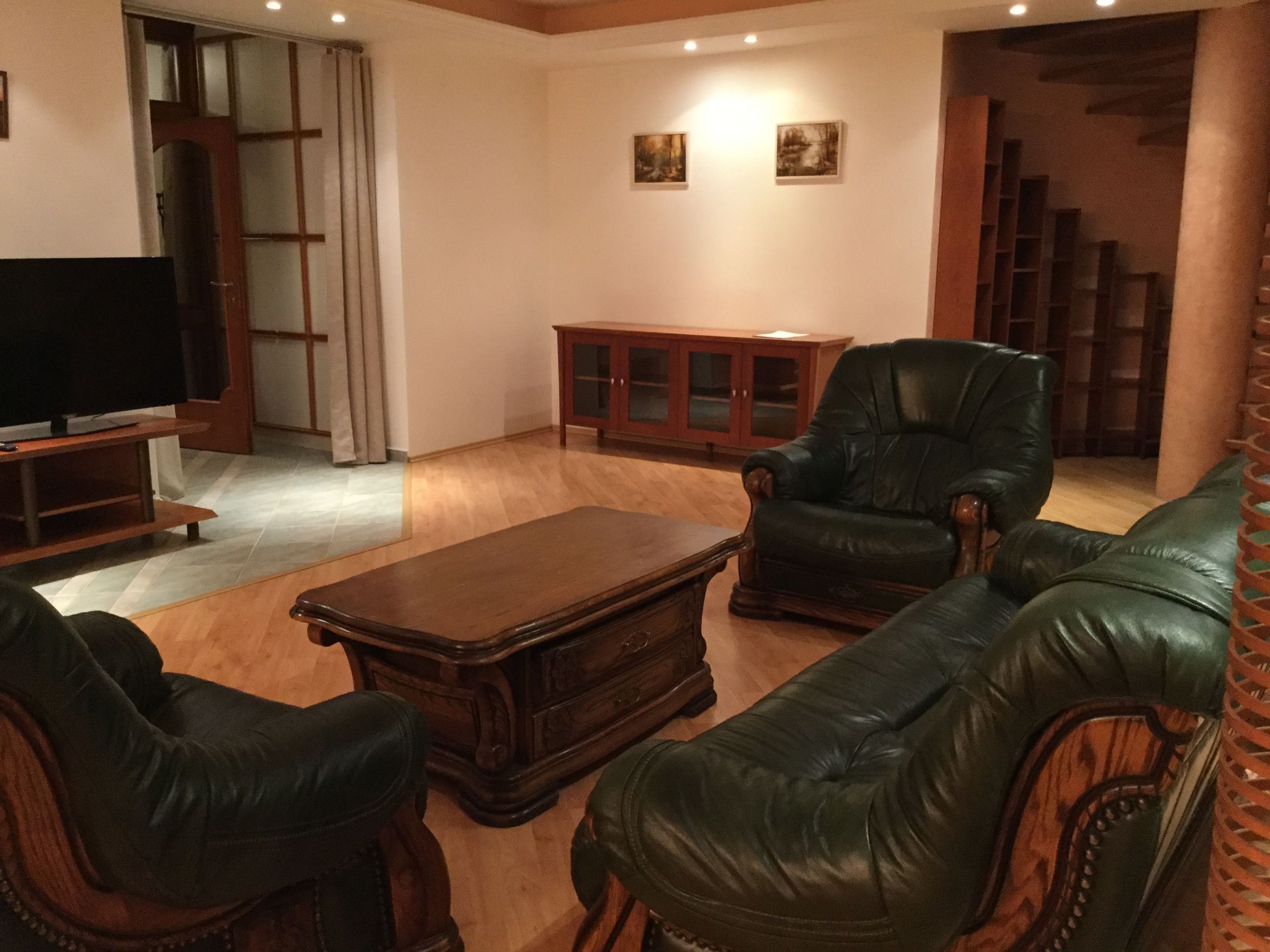 Ein Wohnzimmer mit einer Ledersofa, einem Holztisch und einem Fernseher auf einem Schrank.