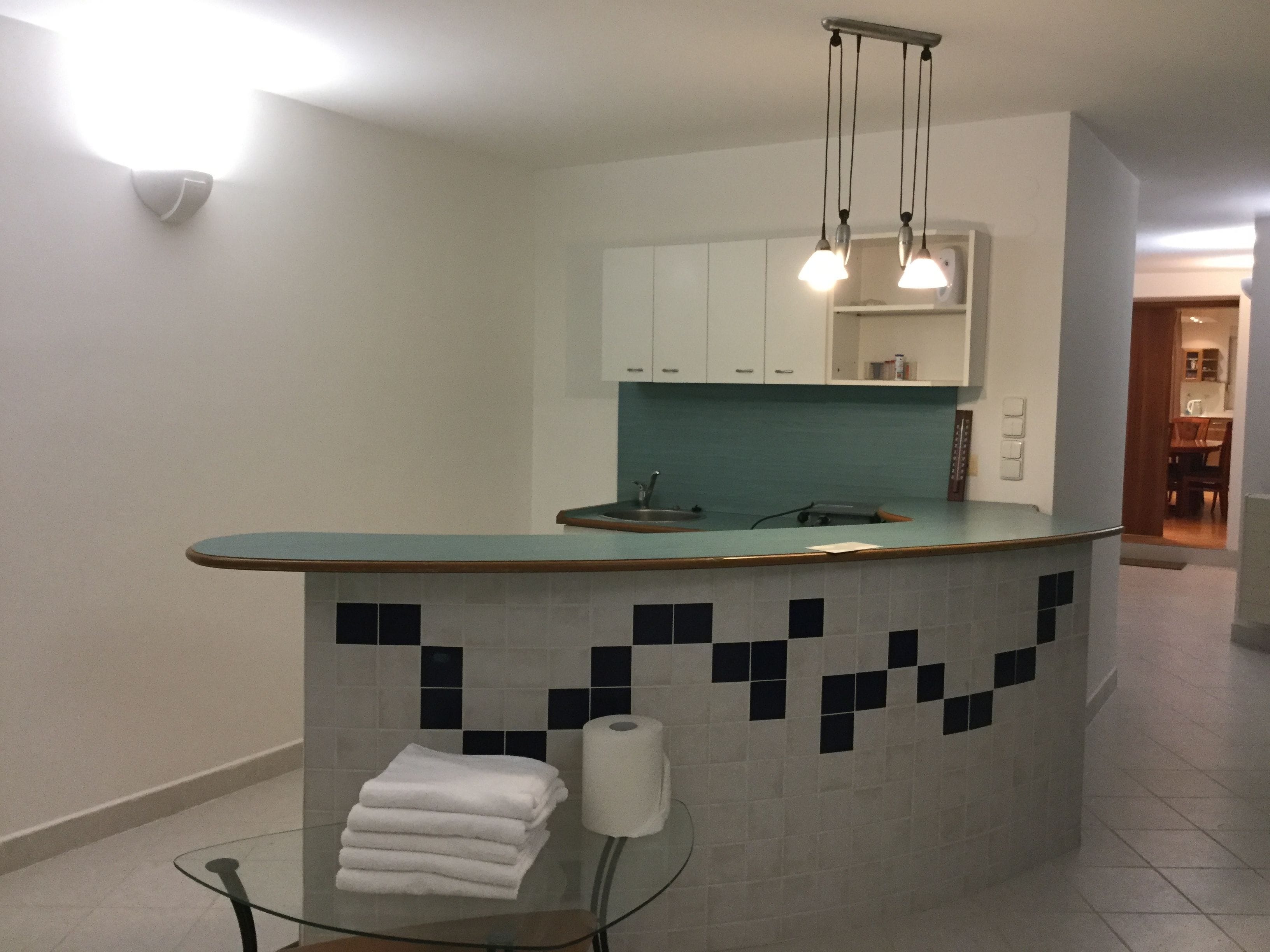 Una cocina moderna con encimera verde azulada, armarios blancos y salpicadero de azulejos.