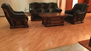 Un salón con suelo de madera, un sofá de cuero verde oscuro, dos sillones de cuero y una mesa de centro de madera.
