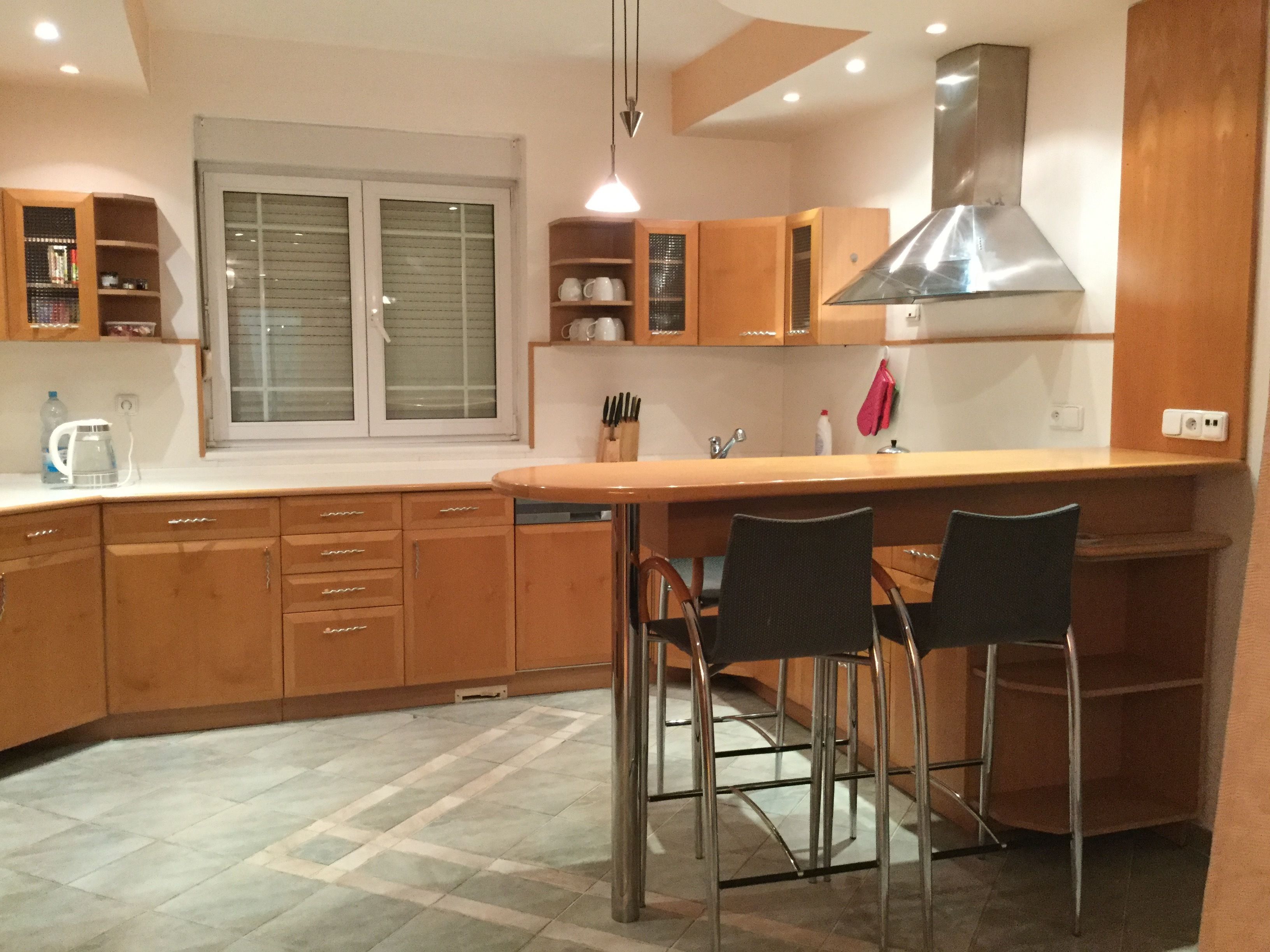 A modern kitchen with wooden cabinets, a stainless steel range hood, and a bar area with two stools.