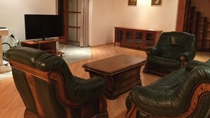 A living room with leather armchairs, a wooden coffee table, a TV on a stand, and a cabinet. - Justyna (Pardubice)