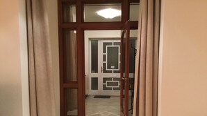 A hallway with a wooden door leading to a room with a patterned wall and a window. - Justyna (Pardubice)