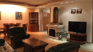 A living room with a fireplace, leather sofas, a television, and a dining area with chairs and a cabinet. - Justyna (Pardubice)