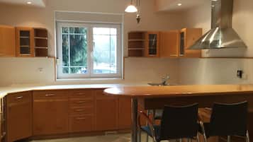 A modern kitchen with wooden cabinets, a large window, and a stainless steel range hood.