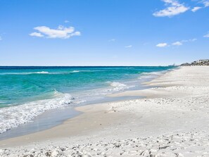 Una playa con agua turquesa cristalina, una orilla arenosa y un edificio a lo lejos.