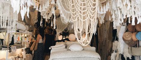 A boutique hotel interior with a central bed area, surrounded by various handmade decor items like macramé and beaded accessories.