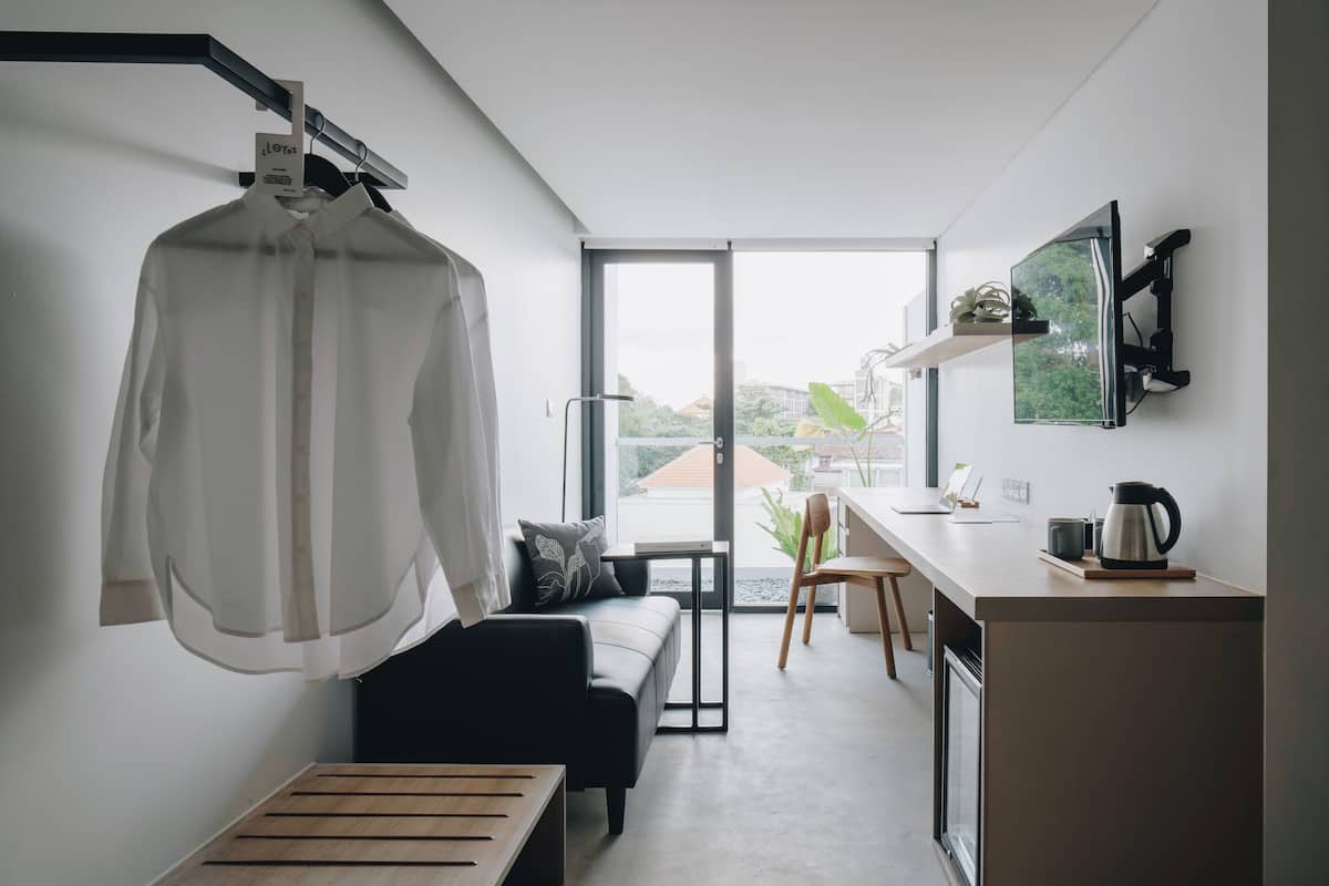 A modern, minimalist living space with a sofa, a coffee table, a dining area with a small table and chairs, and a large window offering a view of the outdoors.