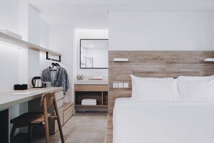 A modern hotel room with a wooden headboard, a desk with a chair, a mirror, and a neatly made bed.