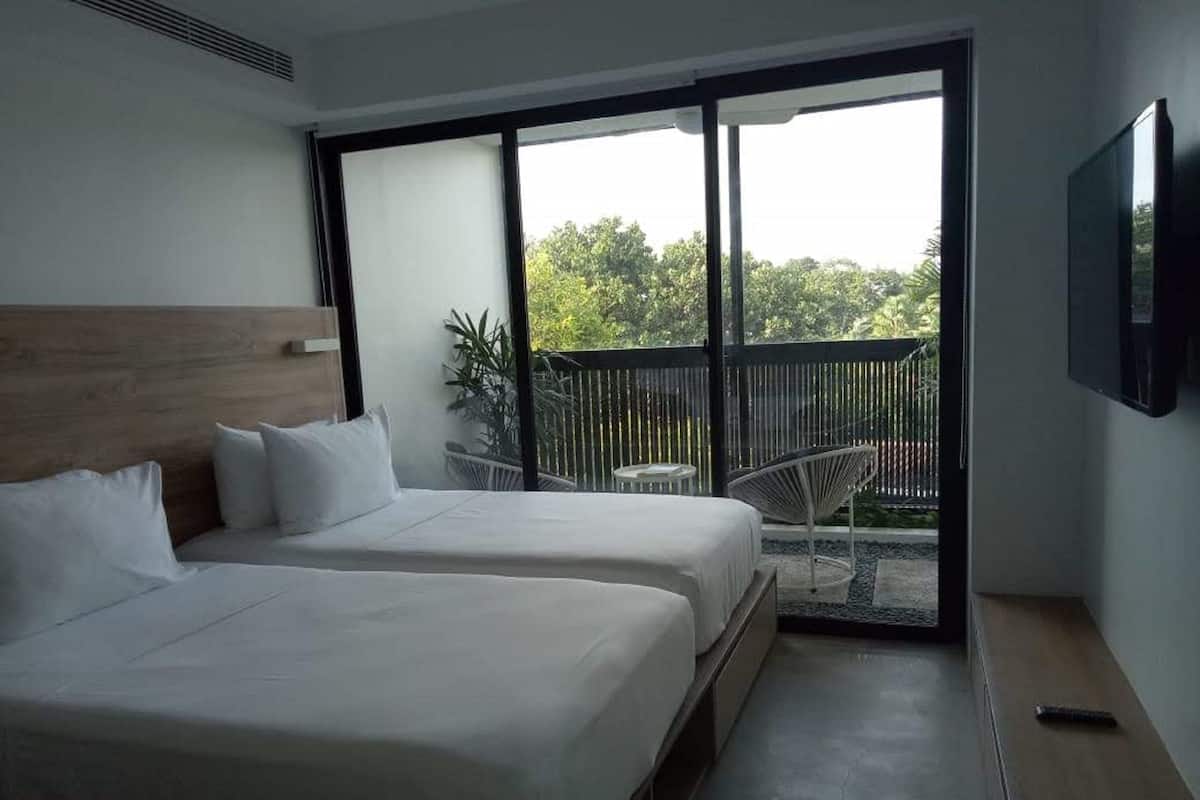 A hotel room with two beds, a balcony, a TV, and a view of greenery.
