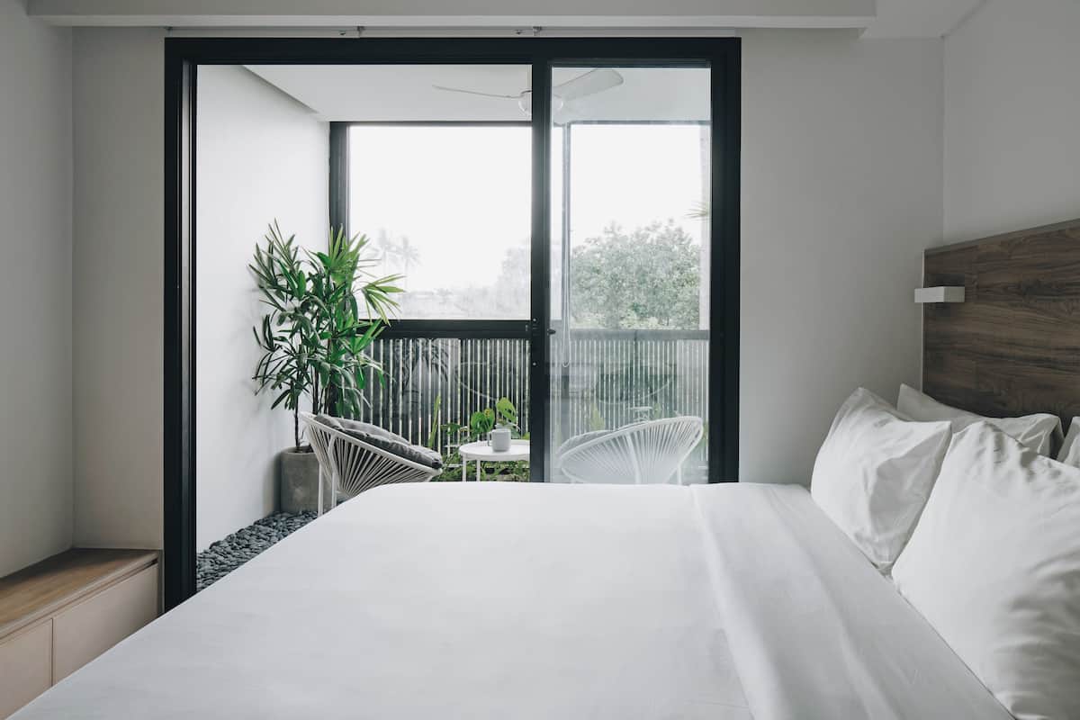 A modern bedroom with a large bed, a balcony with a chair, and a potted plant.