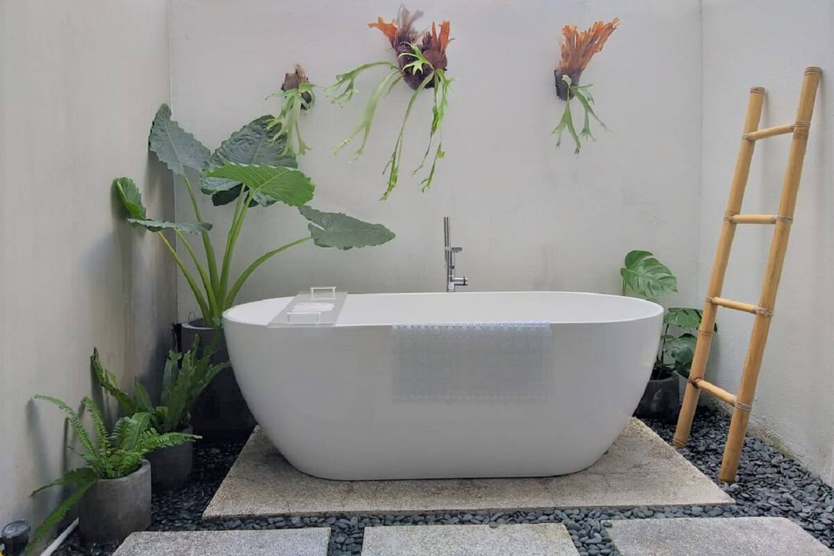 A modern bathroom with a freestanding bathtub, a bamboo ladder, and various potted plants.