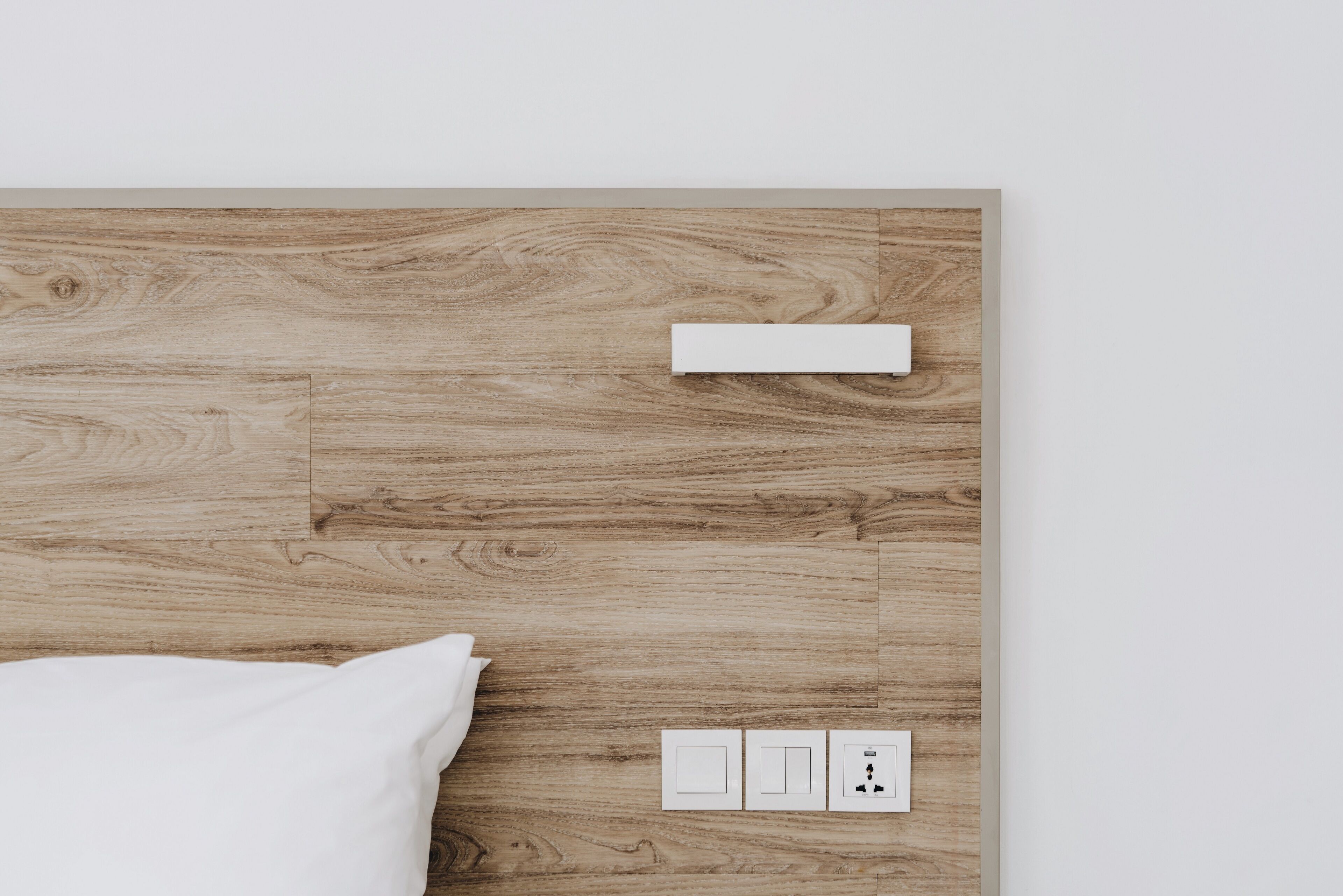 A wooden headboard with a white pillow and a control panel with three switches.