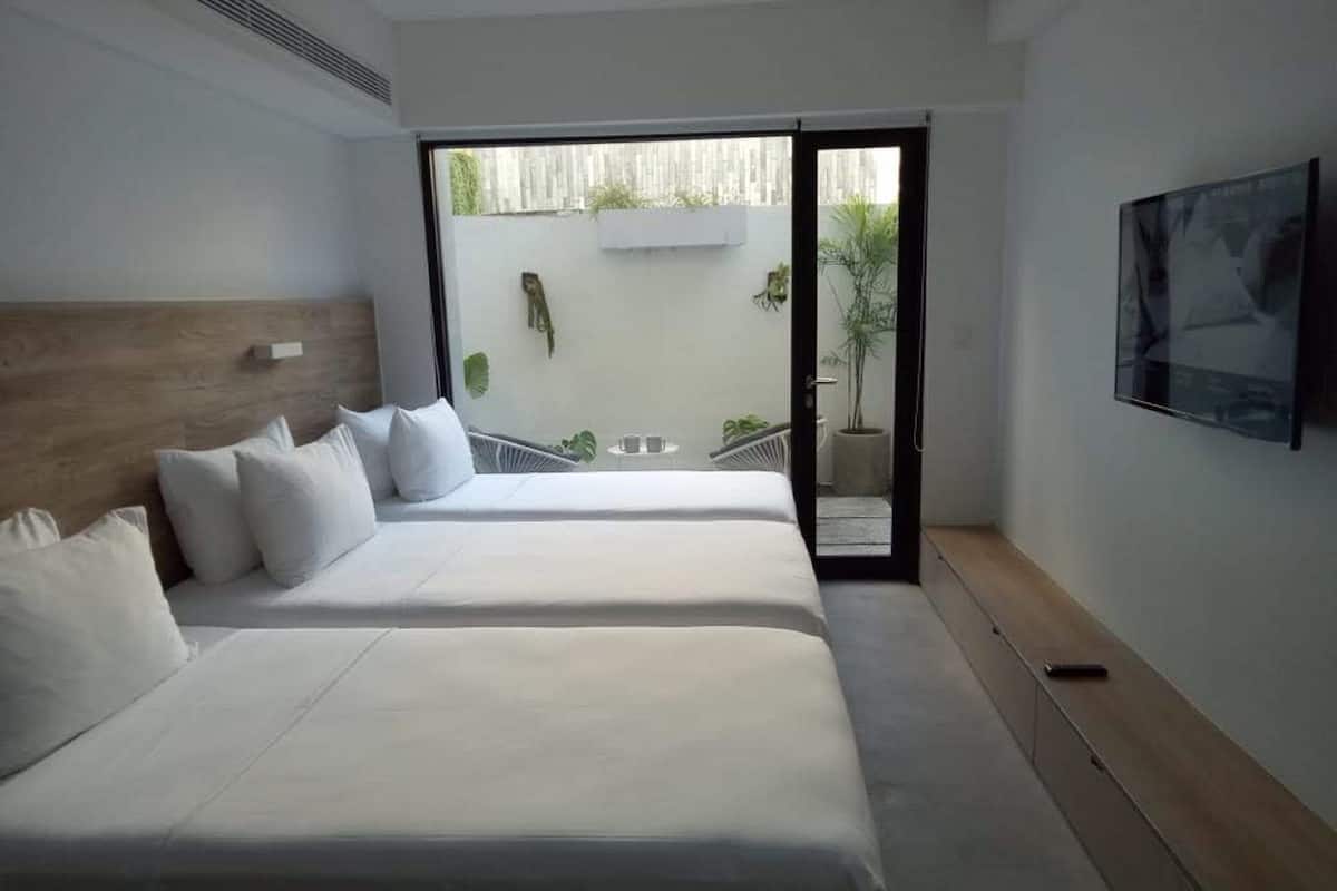 A hotel room with two beds, a TV, and a sliding glass door to an outdoor area.
