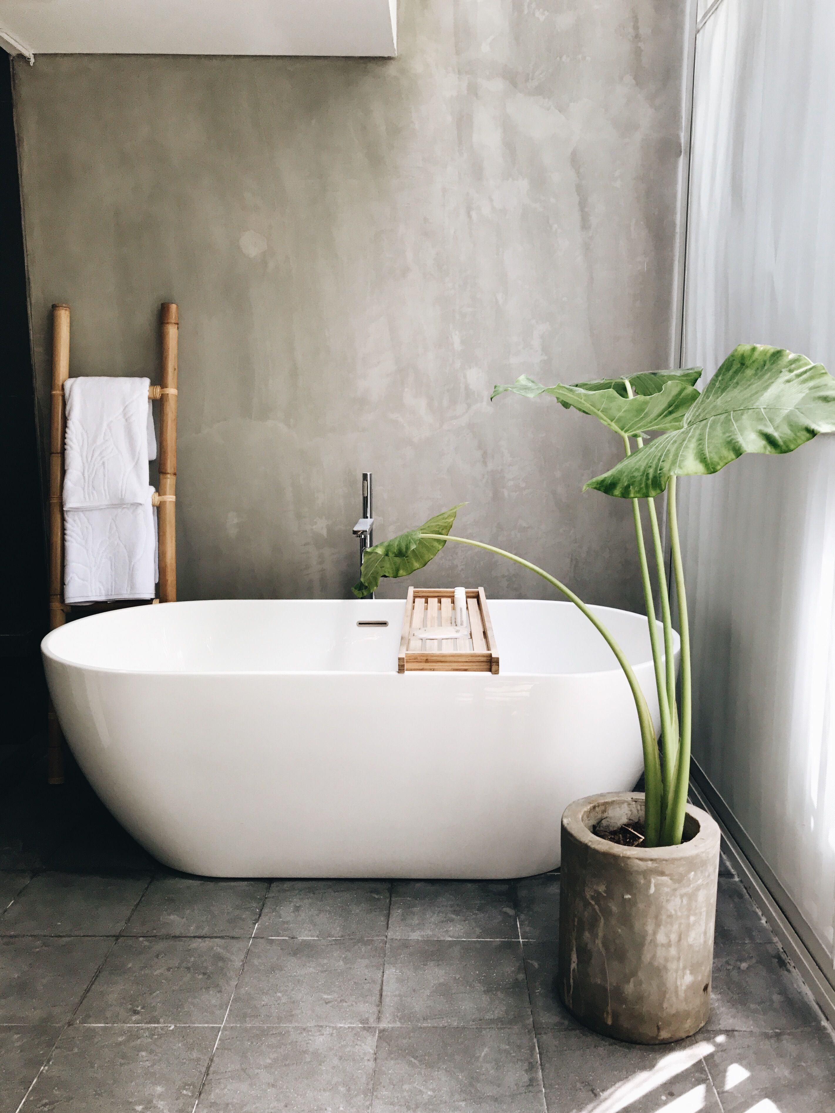 Un baño moderno con una bañera independiente, un perchero de bambú y una planta en maceta.