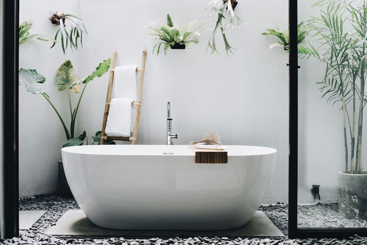A modern bathroom with a freestanding bathtub, bamboo towel rack, and various plants.