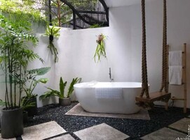 A bathroom with a freestanding bathtub, a hanging plant, and a rope swing.