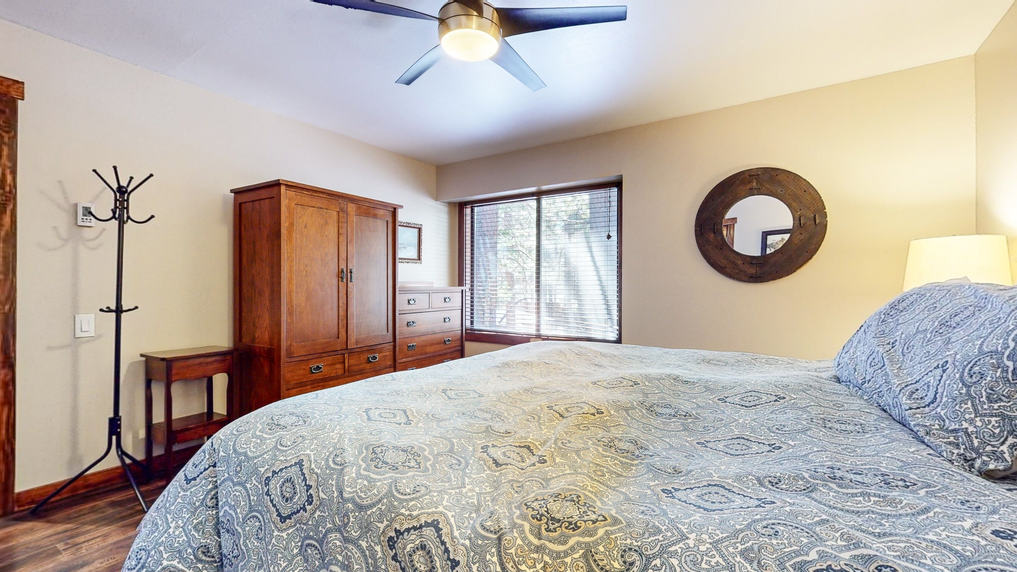 A bedroom with a large bed, a wooden wardrobe, a coat rack, and a ceiling fan.