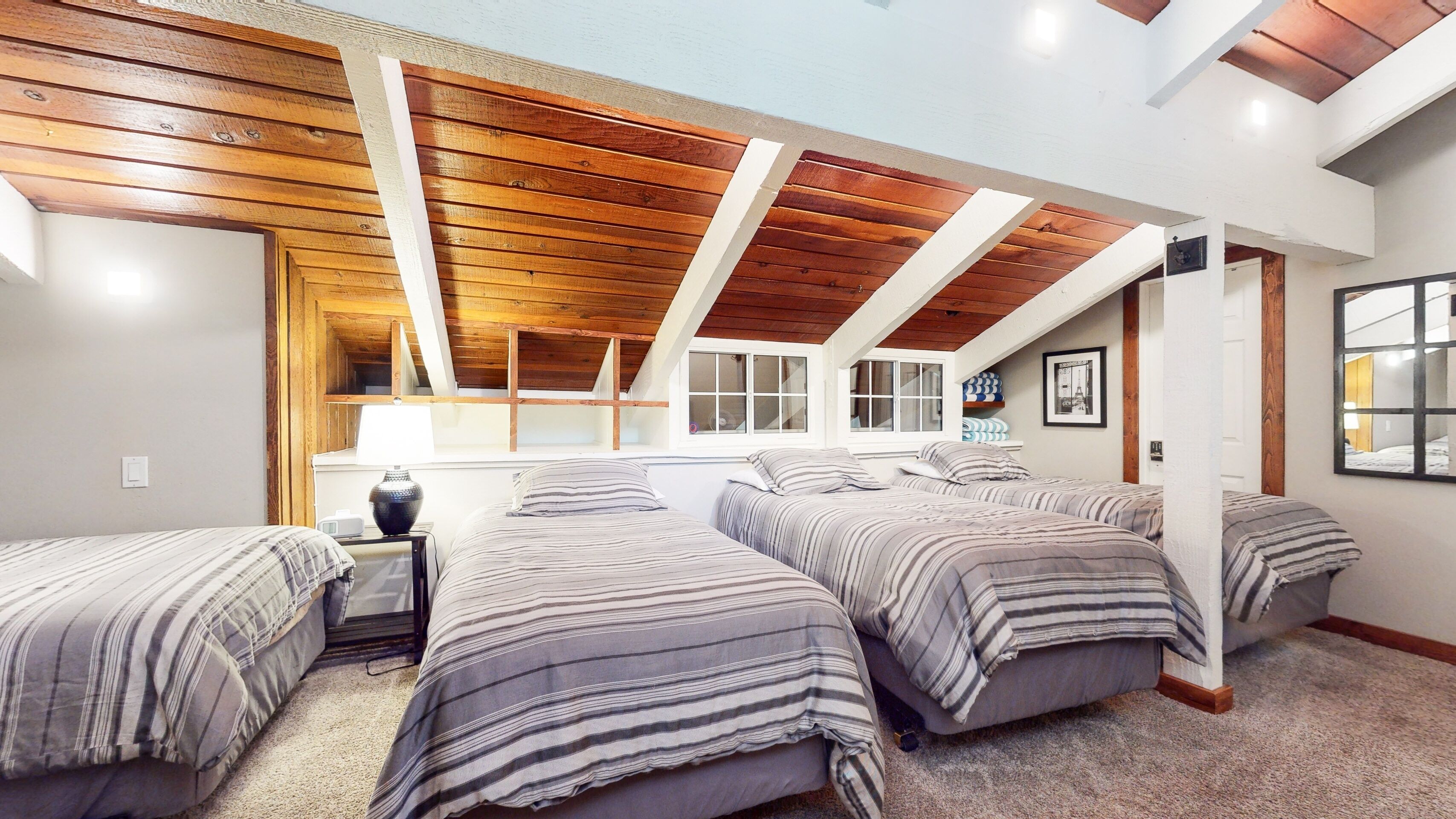 A bedroom with four beds, wooden ceiling beams, and large windows.
