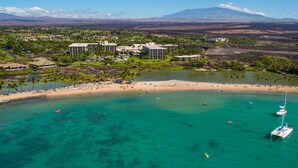 An aerial view of a coastal resort with a sandy beach, clear turquoise waters, and a prominent white yacht anchored near the shore. - Waikoloa Beach S C3 2 Bedroom Villa by RedAwning (Waikoloa)