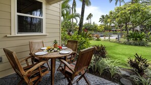 A wooden table set for four with chairs, a window, and a lush garden with palm trees and tropical plants. - Waikoloa Beach S C3 2 Bedroom Villa by RedAwning (Waikoloa)