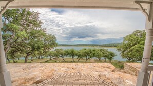 A stone-paved patio with a brick pattern, surrounded by trees and a view of a lake.