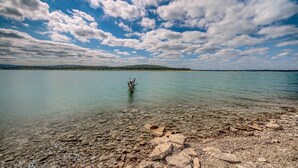 A clear lake with a rocky shore and a distant tree-covered island.
