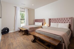 A bedroom with two beds, a wooden bench, a fan, and a window with curtains. - The White House On The Horseshoe 8 Bedroom Home by RedAwning (Canyon Lake)