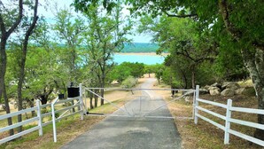 A paved pathway leading to a beach, surrounded by trees and a white fence. - A Shore Thing Cl1105c 1 Bedroom Cottage by RedAwning (Canyon Lake)