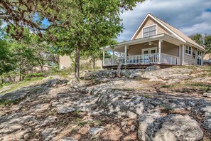 A house with a covered porch, large rocks in the foreground, and trees in the background.