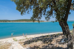 Enjoy a tranquil beach experience with a clear blue sea and a shaded area beneath a large tree.