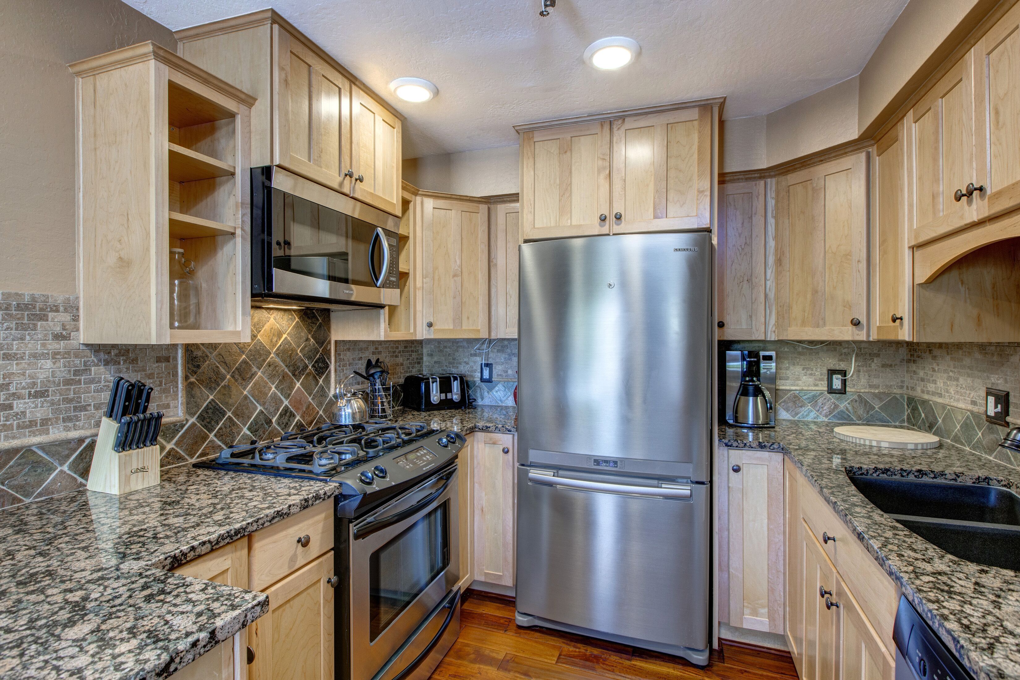 A kitchen with wooden cabinets, granite countertops, a stainless steel refrigerator, a stove, and a microwave.
