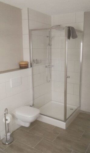Ett modernt badrum med en dusch som är avskärmad med glasväggar, en toalett och ett handfat.