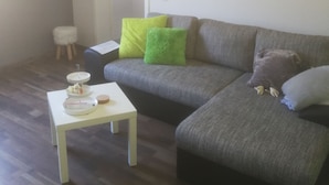 Un salón con un sofá gris, una mesita blanca con una bandeja y un cuadro en la pared.