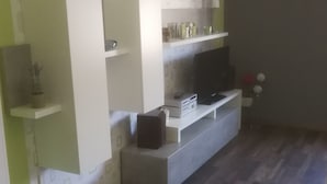 Una sala de estar moderna con televisor empotrado, televisor de pantalla plana sobre un mueble bajo, una pequeña repisa con adornos y una planta en maceta.
