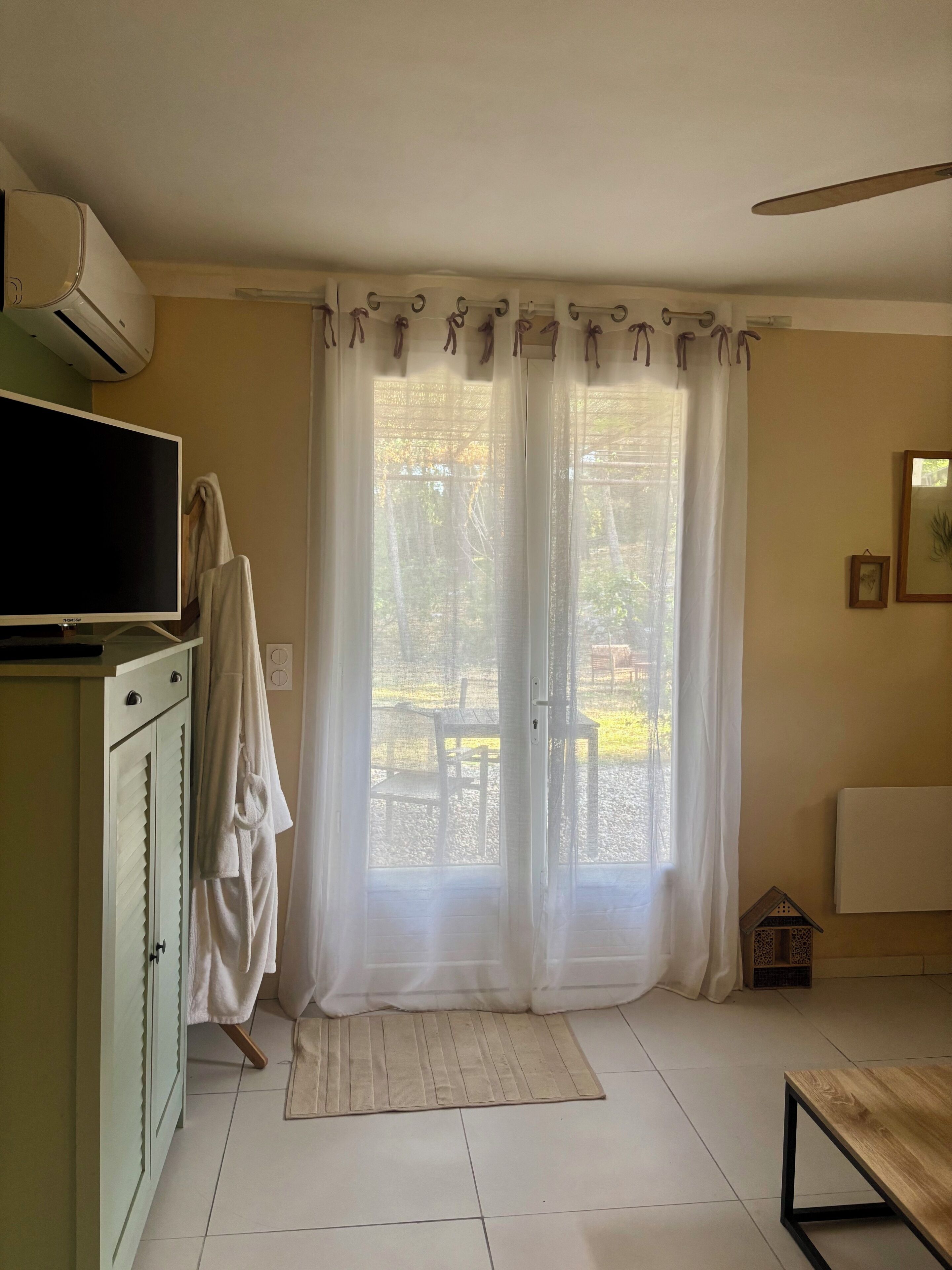A room with a television, a cabinet, a window with curtains, a small table, and a radiator.
