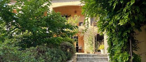 Una escalera de piedra conduce a un edificio con techo de tejas, rodeado de follaje y un jardín.