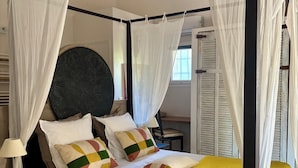 Een hemelbed met wit baldakijn, een rond decoratief hoofdeinde en een gele sprei.