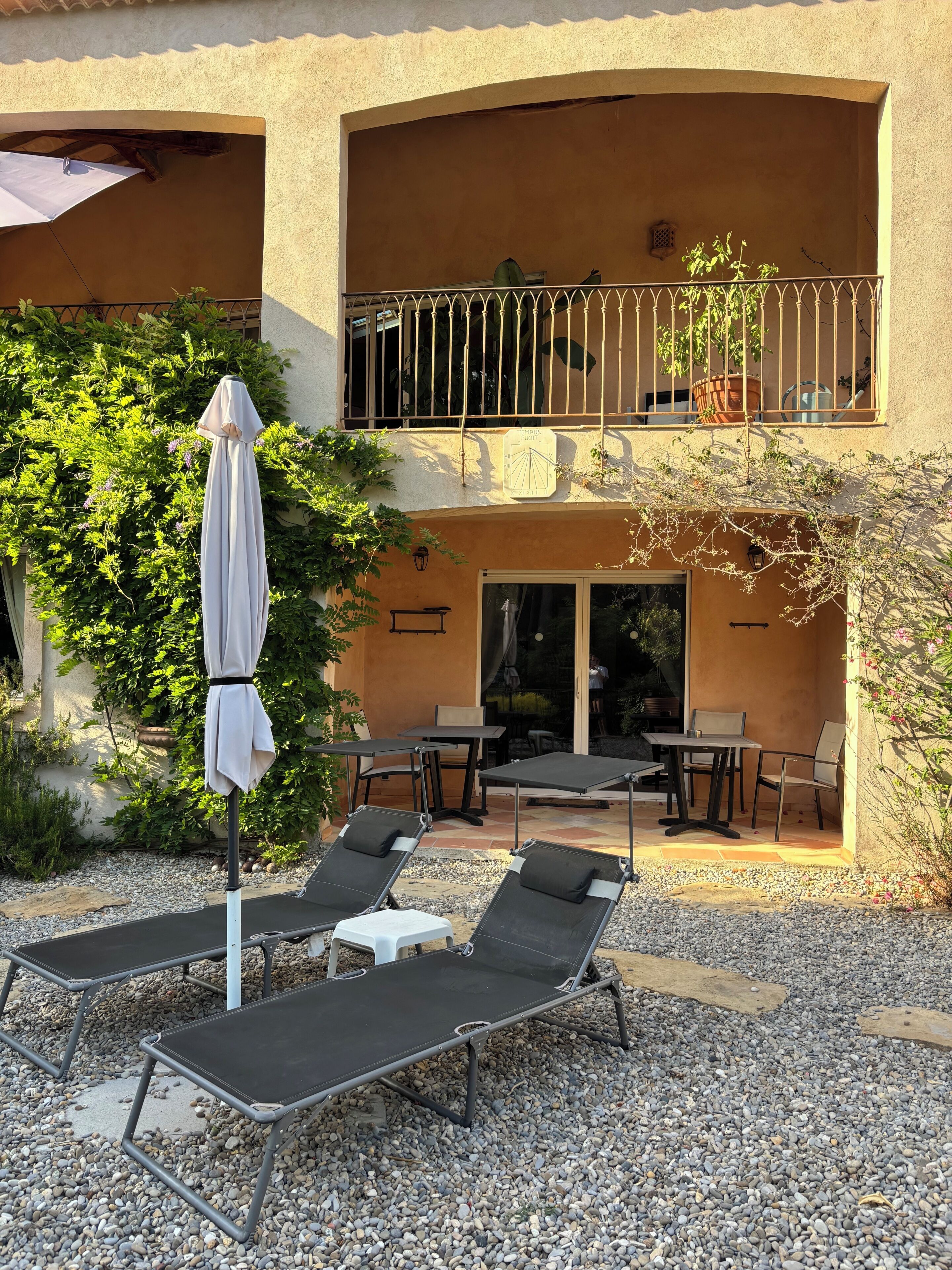 A building with a balcony, outdoor seating area with lounge chairs and tables, and a covered umbrella.