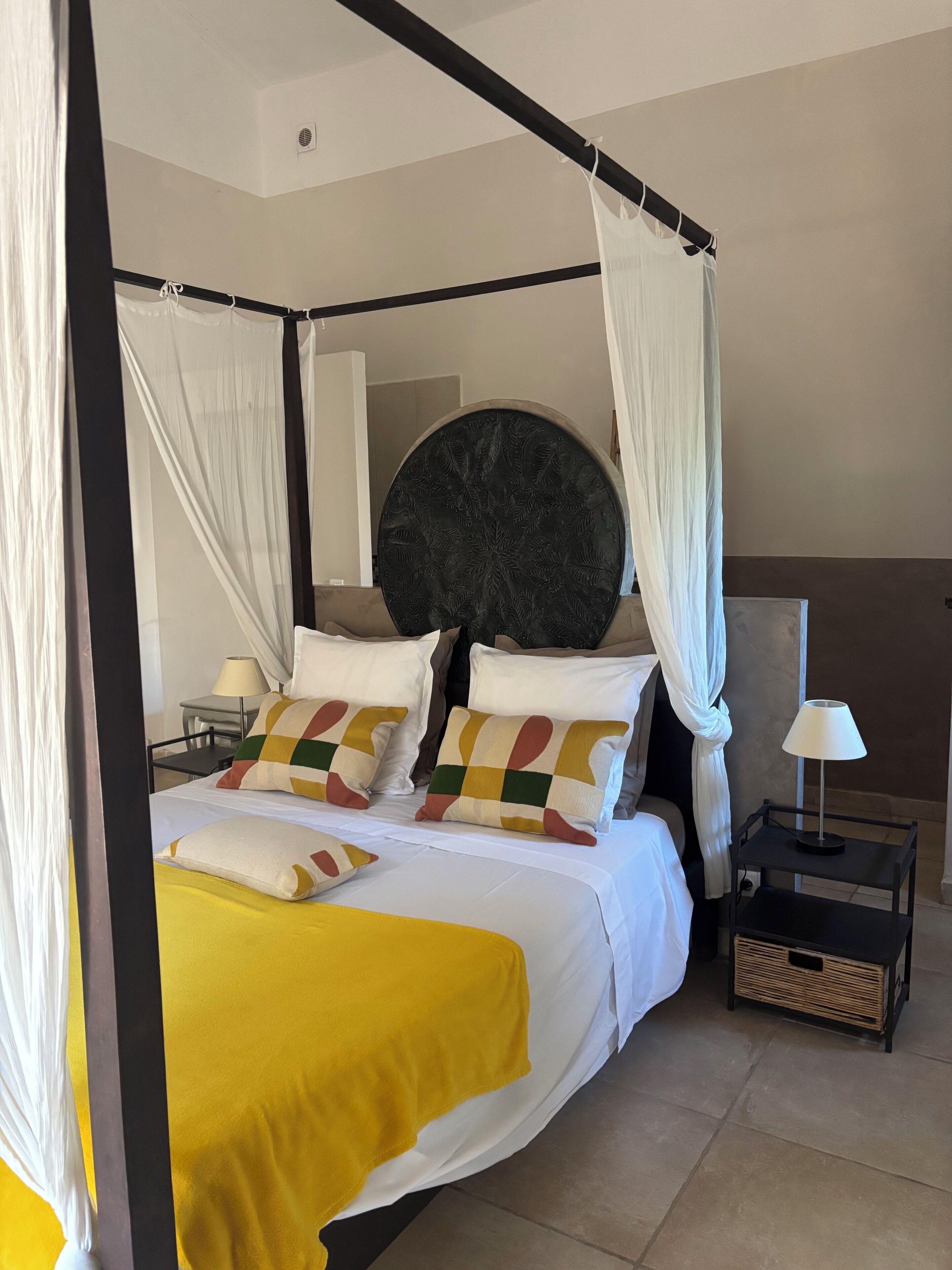 A four-poster bed with a canopy, a round decorative wall piece, and a bedside table with a lamp.